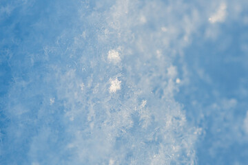 Close-up view of delicate snow crystals sparkling in the sunlight on a clear blue winter day, showcasing the intricate beauty of nature's frozen artistry