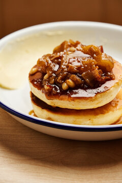 Fluffy pancakes are stacked high and generously topped with sweet caramelized apples and crunchy pine nuts on a rustic plate, inviting the perfect brunch experience at a cozy cafe