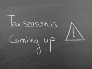 Handwritten text on a chalkboard stating "Tax season is coming up!", with an exclamation mark in a triangle