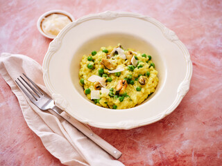 A bowl of creamy risotto is presented with fresh peas and mussels. A fork rests beside the bowl on a light linen napkin, enhancing the inviting meal setting