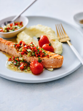 Cooked salmon fillet is beautifully plated with creamy mashed potatoes and roasted cherry tomatoes. The dish showcases vibrant colors and textures, perfect for a delightful meal