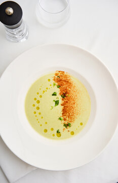 A beautifully arranged bowl of gourmet soup shows a creamy base accented by a sprinkle of seasoning and a swirl of oil. The presentation highlights culinary artistry in a fine dining atmosphere
