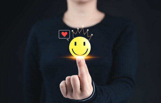 Positive emotion and mental well-being concept. A woman touching a glowing smile face with a crown and heart icon, symbolizing happiness, mental well-being, positive feedback, and emotional health.