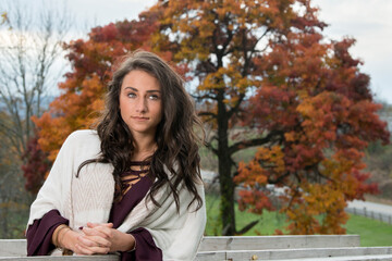 Cute young brunette woman poses for photo leaning on wooden railing