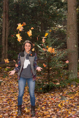 Cute young brunette woman poses for photo in forest playfully throwing leaves