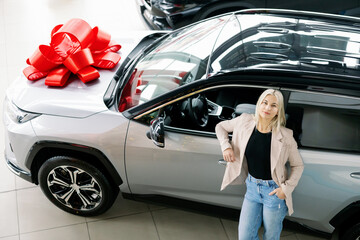 Woman Leaning on New Car with Red Bow in Dealership