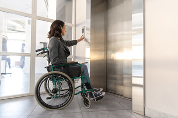 Female entrepreneur with disabilities in wheel chair waiting for elevator in office at work