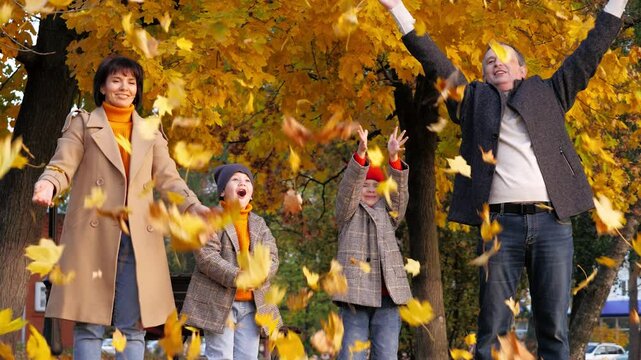 Family throws up autumn leaves in city park on common weekend. Father mother and children joyfully toss golden leaves on vocation. Happy family shows playful leaf-throwing tradition on autumn day