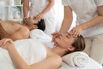 Caucasian couple enjoying relaxing anti-stress head massage and pampering facial beauty skin recreation leisure in dayspa modern light ambient at luxury resort or hotel spa salon. Quiescent