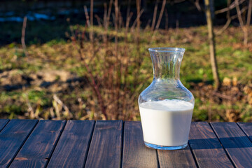 Glass bottle with white milk on wooden table, closeup, outdoors. Fresh milk for drinking