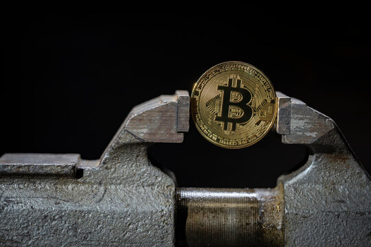 Metal golden bitcoin under pressurein old vise grip, closeup. Concept of cryptocurrency strength