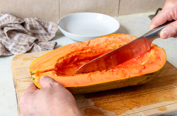 A person slicing a half papaya with the seeds cleaned out.