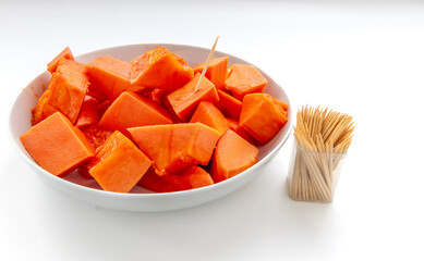 Sweet soft cut pieces of ripe papaya served on a plate with wooden picks isolated on white.