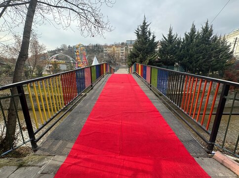 A red carpet has been laid on the metal bridge with colorfully painted iron railings. The iron bridge connecting the two sides of the city. The rainbow-colored bridge and the red carpet. Close-up.