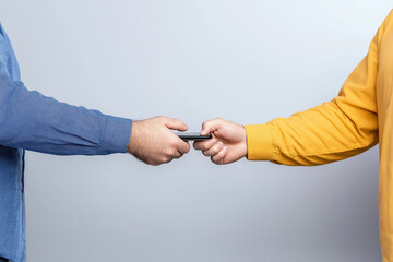 Two people exchanging a smartphone against a gray background in a casual setting