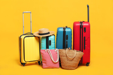 Many colorful suitcases, beach bags and straw hat on orange background