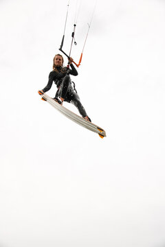 Kite surfer woman holding on to the handle of the kite with one hand while flying in the air