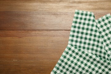 Green checkered tablecloth on wooden background, top view. Space for text