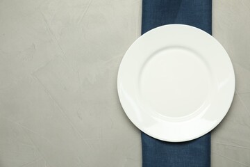 Blue napkin and empty plate on grey table, top view. Space for text