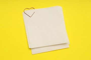 Heart shaped paper clip and notes on yellow background, top view. Space for text