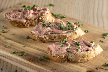 Three slices of spreadable pâté made with red onion and butter on rustic bread on wooden cutting board.