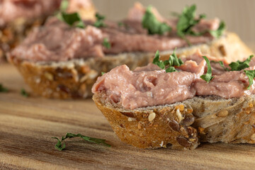 Slices of spreadable pâté made with red onion and butter on rustic bread on wooden cutting board. Close up view.