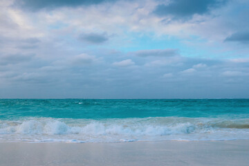 Obraz premium Breaking beach waves along turquoise ocean with cloudy skies and a clearing of blue sky 