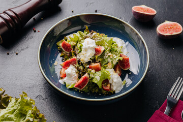 Fresh fig and burrata salad with leafy greens, almonds, and creamy dressing in a rustic blue bowl