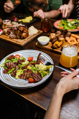 A person holds a fork with a bite, while beer and various dishes on a table.
