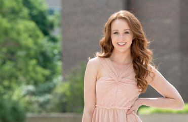 Naklejka premium Stunning young woman with red hair poses for photo on campus wearing pink blouse and blue jeans