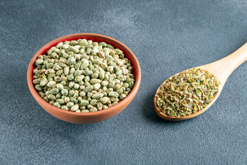 A bowl filled with a pile of natural dried thyme seeds, alongside a spoon containing ground thyme
