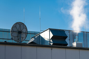 A rooftop equipped with various structures including ventilation ducts, a satellite dish, and smoke...