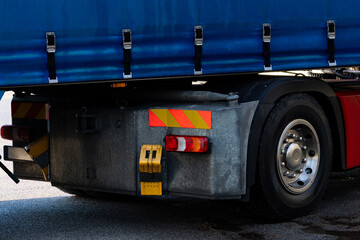 Rear view of wheel and brake light of large truck parked at a loading dock features a blue tarp covering its cargo.
