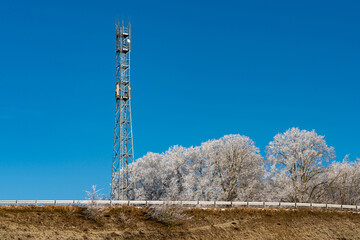A communication tower rises prominently beside a frost-covered landscape. The bright blue sky...