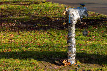 A fire hydrant wrapped in grey tape stands on a grassy area in a park. The ground is covered with...