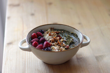 Beige bowl with green smoothie, frozen berries and homemade granola, served on the table. Selective focus.