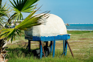 An abandoned stone oven under palm trees on the seashore.