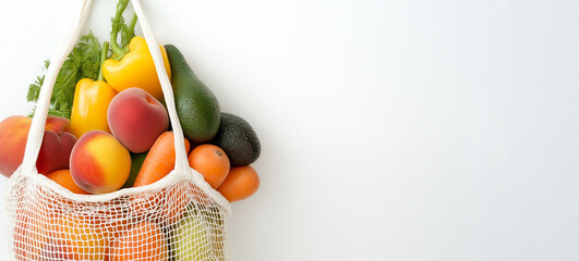 Reusable mesh shopping bag containing a mix of fresh produce like avocados, carrots, and peaches, hanging on a white background promoting healthy eating habits and sustainability