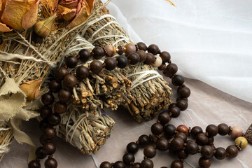 White sage smudge sticks with wooden mala prayer beads on a soft white fabric.  One of the smudge...