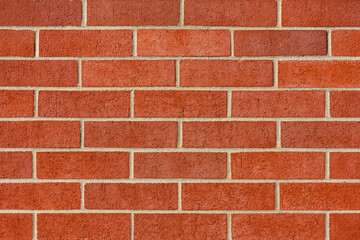 An abstract image of a rectangular red brick exterior wall with a rough texture and varying shades of red ranging from light to dark. 