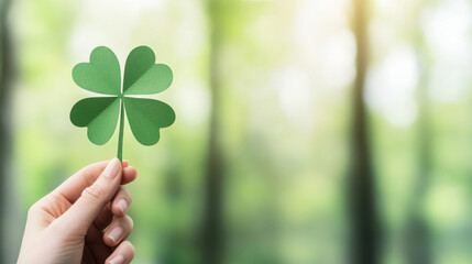 Holding paper four-leaf clover cutout over soft forest backdrop, symbolizing Irish luck, natural serenity, minimalist St. Patrick's Day composition with negative space
