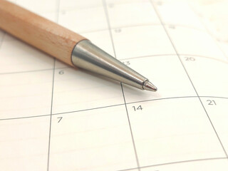 Closeup view of a wooden ballpoint pen resting on a calendar, symbolizing planning, scheduling, and organization for important dates, appointments, and deadlines.
