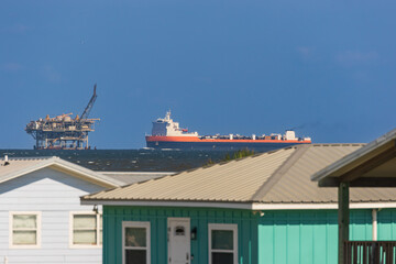 oil platform and large cargo ship in the distance from homes at the coast with a blurred foreground and haze. 