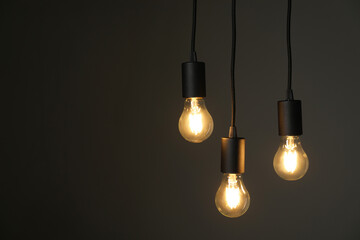 Light bulbs hanging on cords against grey background, space for text