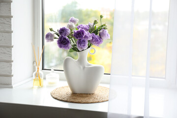 Stylish vase with beautiful flowers, candle and reed diffuser near window at home