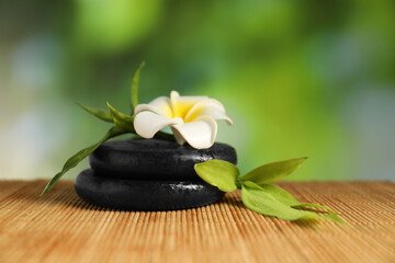 Spa stones, plumeria flower and green leaves on bamboo mat