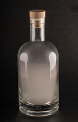 A clear 750ml glass bottle, typically used for spirits, is filled with swirling white smoke. The bottle features a wooden cork and sits against a dramatic black background.