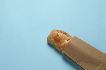 Paper bag with fresh baguette on light blue background, top view. Space for text