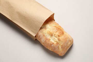 Paper bag with fresh baguette on light gray table, top view