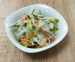 Fresh vegetable salad with clear noodles served in a white bowl on wooden table